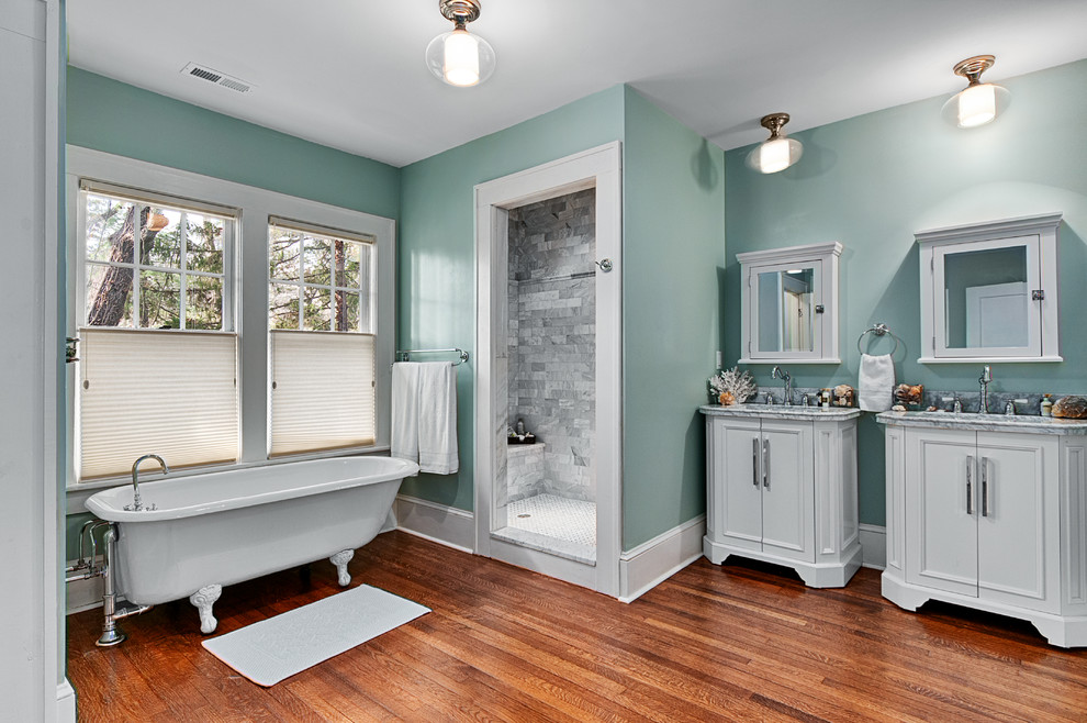 Bild på ett vintage grå grått badrum, med vita skåp, ett badkar med tassar, en dusch i en alkov, blå väggar, mellanmörkt trägolv, grå kakel och luckor med infälld panel