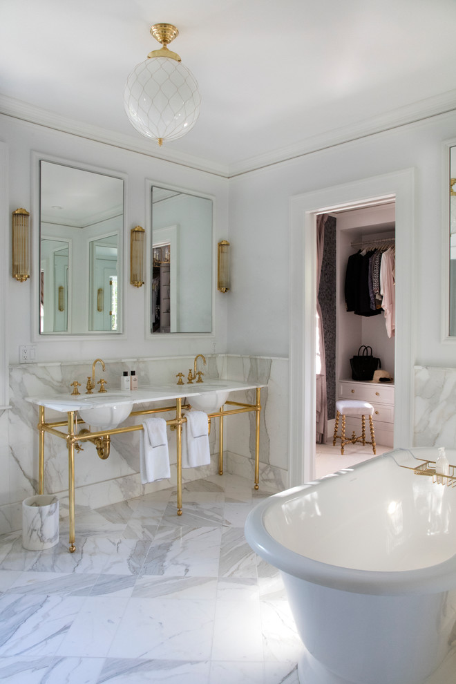 На фото: главная ванная комната в стиле неоклассика (современная классика) с отдельно стоящей ванной, белыми стенами, мраморным полом, мраморной столешницей, белой плиткой, раковиной с пьедесталом и зеркалом с подсветкой