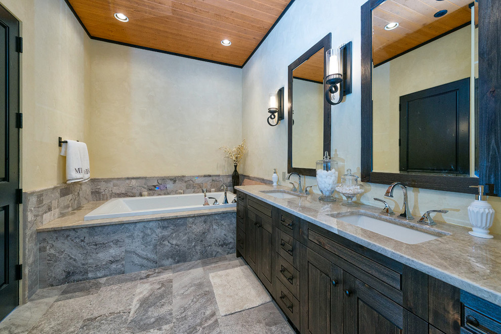 Cette photo montre une salle de bain chic en bois foncé avec un lavabo encastré, un placard à porte shaker, une baignoire posée et un carrelage gris.