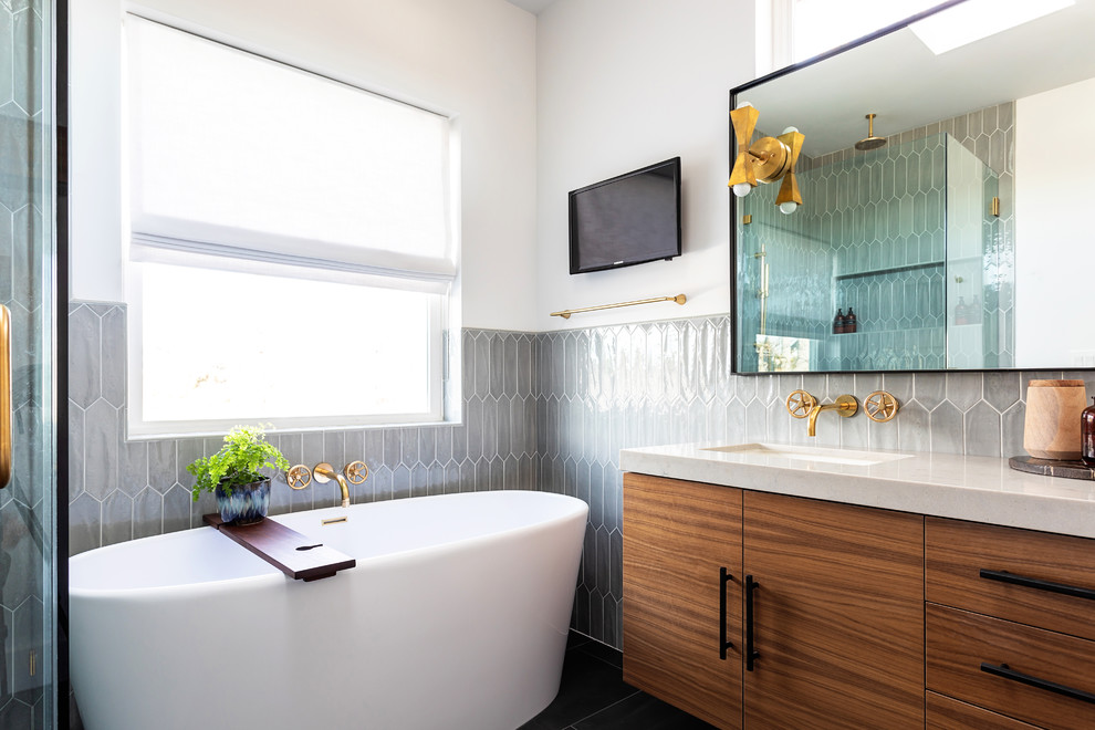 Идея дизайна: ванная комната в стиле неоклассика (современная классика) с плоскими фасадами, фасадами цвета дерева среднего тона, отдельно стоящей ванной, серой плиткой, белыми стенами, врезной раковиной, черным полом и бежевой столешницей