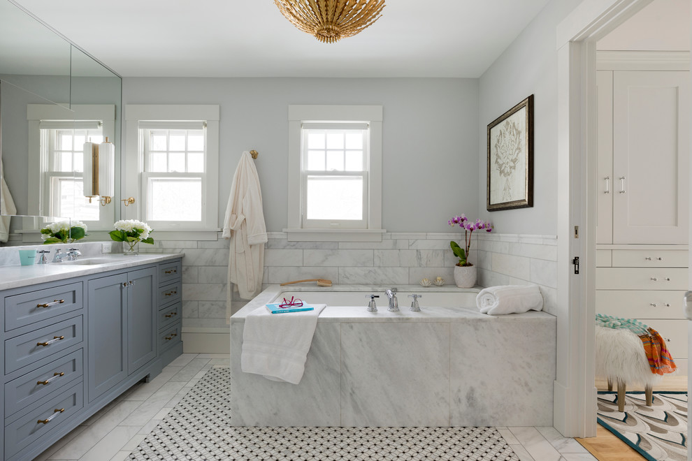 Inspiration pour une salle de bain traditionnelle avec un placard à porte shaker, des portes de placard grises, une baignoire encastrée, un carrelage blanc, un mur gris, un lavabo encastré, un sol blanc et un plan de toilette blanc.