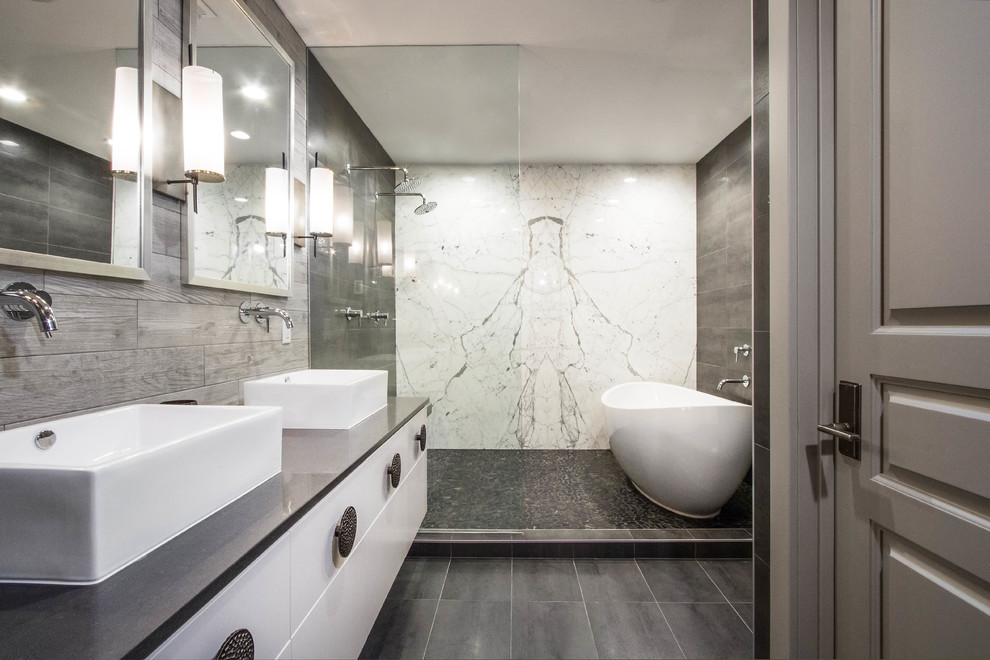 Klassisk inredning av ett grå grått en-suite badrum, med släta luckor, vita skåp, ett fristående badkar, våtrum, grå kakel, ett fristående handfat, grått golv och med dusch som är öppen