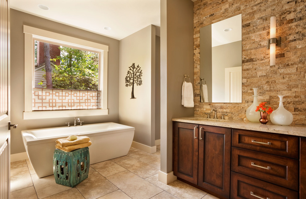 Immagine di una stanza da bagno chic con lavabo sottopiano, ante in stile shaker, ante in legno bruno, vasca freestanding e piastrelle in pietra