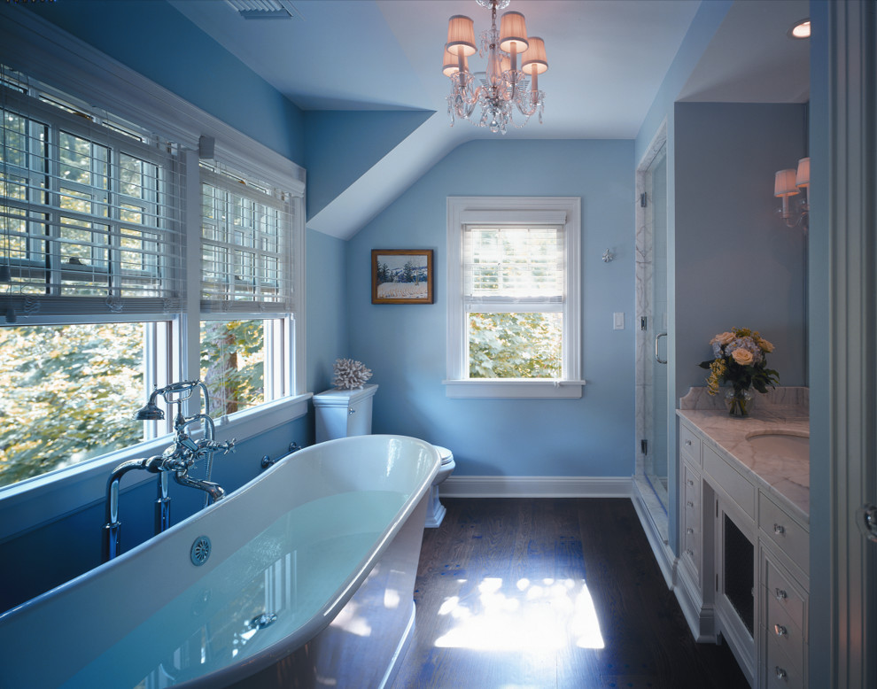 Bild på ett stort vintage en-suite badrum, med ett undermonterad handfat, luckor med infälld panel, beige skåp, marmorbänkskiva, ett fristående badkar, en dusch i en alkov, en toalettstol med separat cisternkåpa, blå väggar och mörkt trägolv