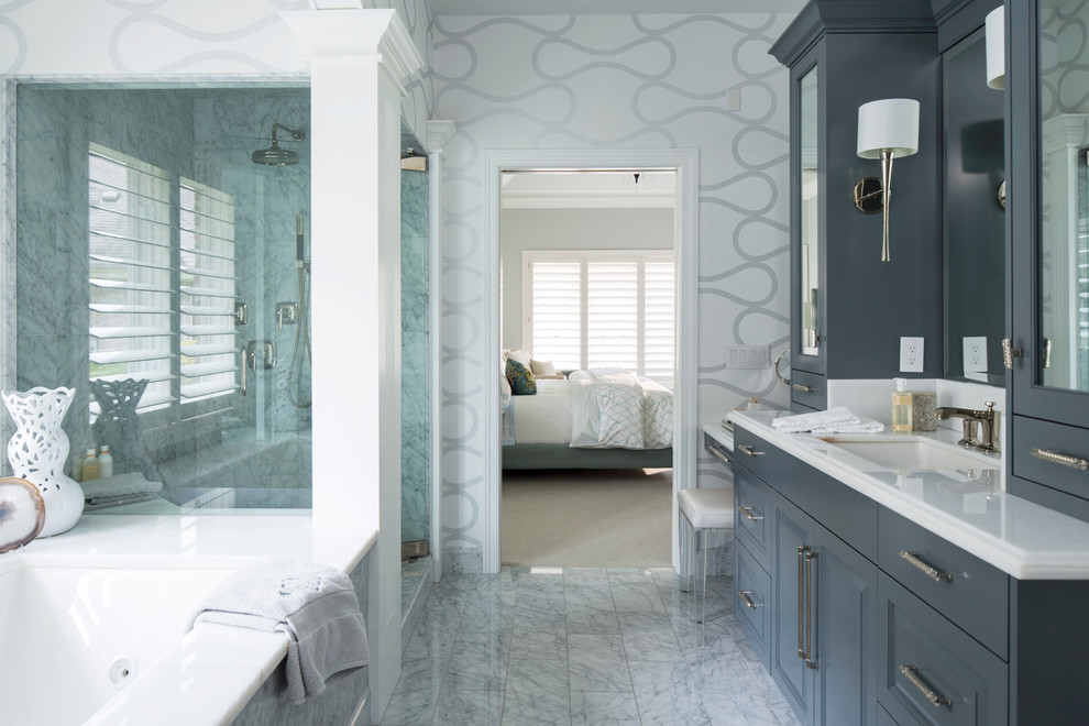 Cette image montre une salle de bain principale traditionnelle avec un lavabo encastré, un placard avec porte à panneau surélevé, une baignoire encastrée, un mur multicolore, un carrelage blanc, un sol en marbre et des portes de placard bleues.
