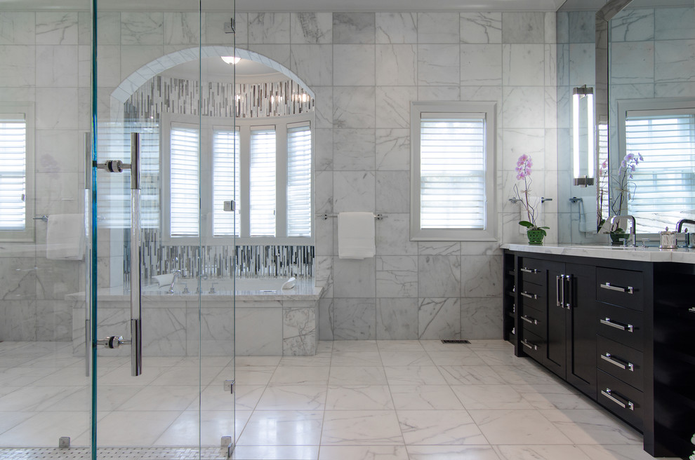 Cette image montre une salle de bain traditionnelle avec un placard à porte plane, des portes de placard noires, un plan de toilette en marbre, une baignoire posée et une douche double.