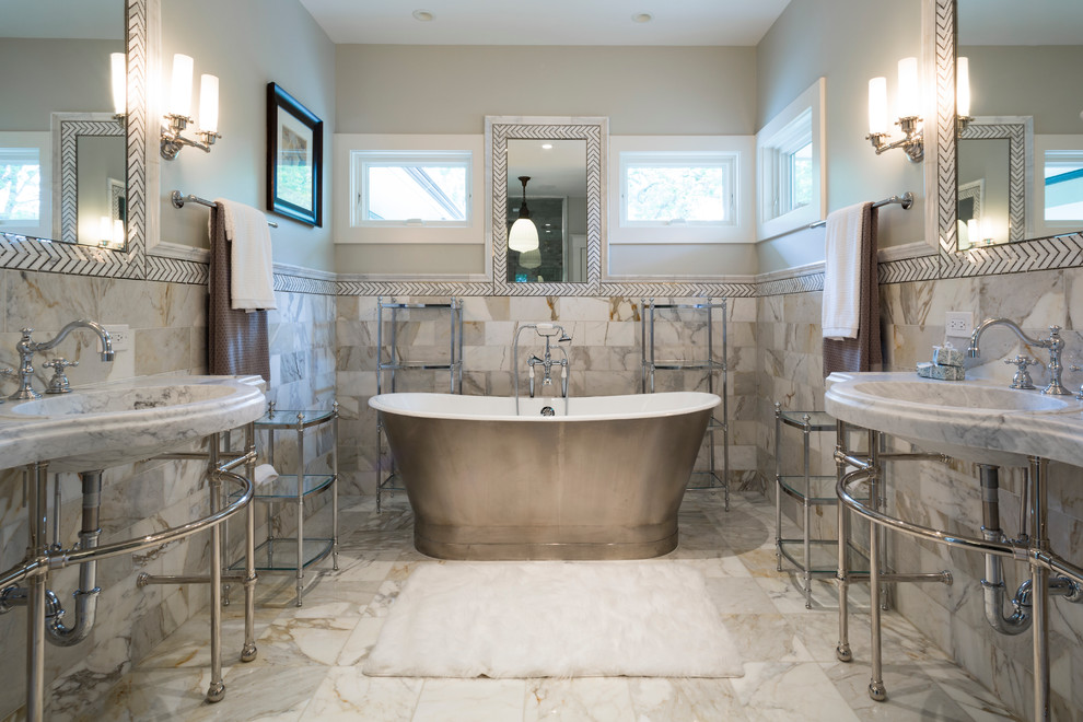 Cette image montre une grande salle de bain principale traditionnelle avec un lavabo intégré, un plan de toilette en marbre, une baignoire indépendante, un carrelage de pierre, un mur gris, un sol en marbre et un carrelage gris.