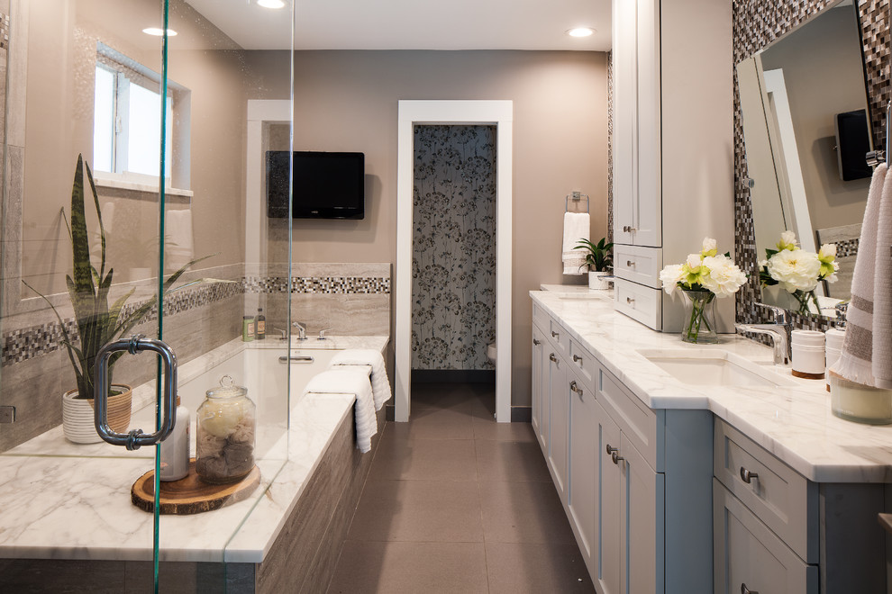 Example of a mid-sized beach style master beige tile and mosaic tile porcelain tile and gray floor corner shower design in Miami with recessed-panel cabinets, gray cabinets, an undermount tub, a two-piece toilet, gray walls, an undermount sink, marble countertops, a hinged shower door and white countertops
