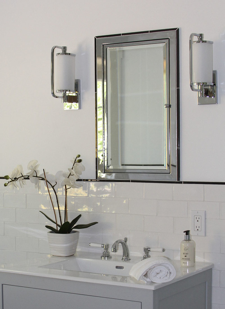 Cette image montre une salle de bain principale traditionnelle de taille moyenne avec des portes de placard grises, un carrelage blanc, un lavabo intégré, un placard à porte plane, un carrelage métro, un mur blanc et un plan de toilette en surface solide.
