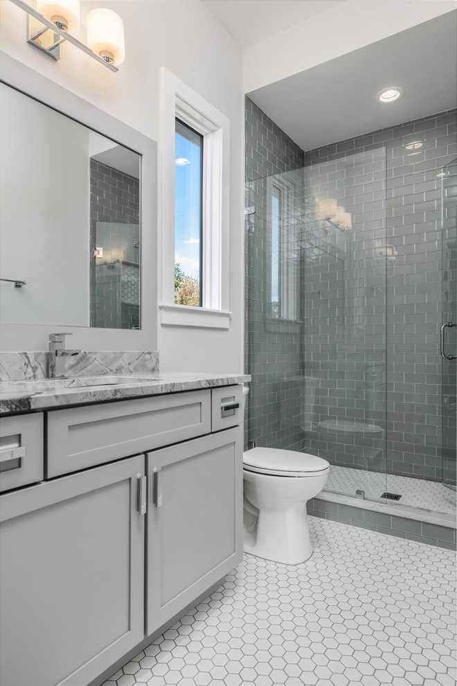 Exemple d'une salle de bain chic de taille moyenne avec un placard à porte shaker, des portes de placard grises, WC à poser, un carrelage gris, un carrelage métro, un mur gris, un sol en carrelage de céramique, un lavabo encastré, un plan de toilette en marbre, un sol blanc, une cabine de douche à porte battante et un plan de toilette gris.