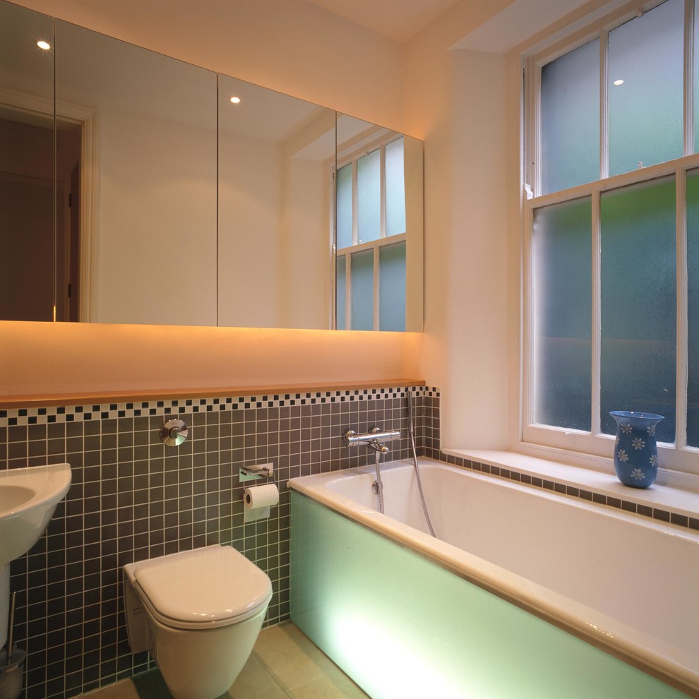 Inspiration for a mid-sized contemporary kids' multicolored tile and porcelain tile limestone floor drop-in bathtub remodel in London with a wall-mount toilet, white walls, a wall-mount sink, quartz countertops and glass-front cabinets