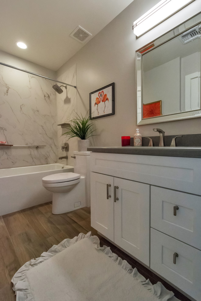 Photo of a medium sized classic family bathroom in Phoenix with raised-panel cabinets, white cabinets, an alcove bath, a shower/bath combination, a one-piece toilet, grey walls, porcelain flooring, a built-in sink, quartz worktops, brown floors and a shower curtain.