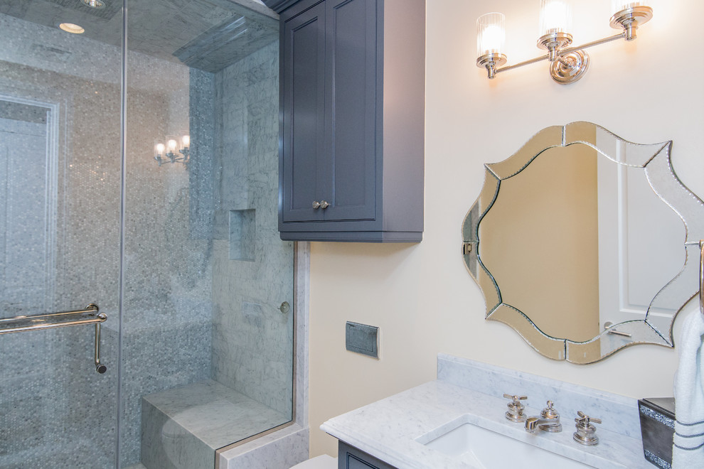 Idées déco pour une salle de bain classique de taille moyenne avec un placard avec porte à panneau encastré, des portes de placard grises, un carrelage gris, un carrelage de pierre, un mur beige, un lavabo encastré et un plan de toilette en marbre.