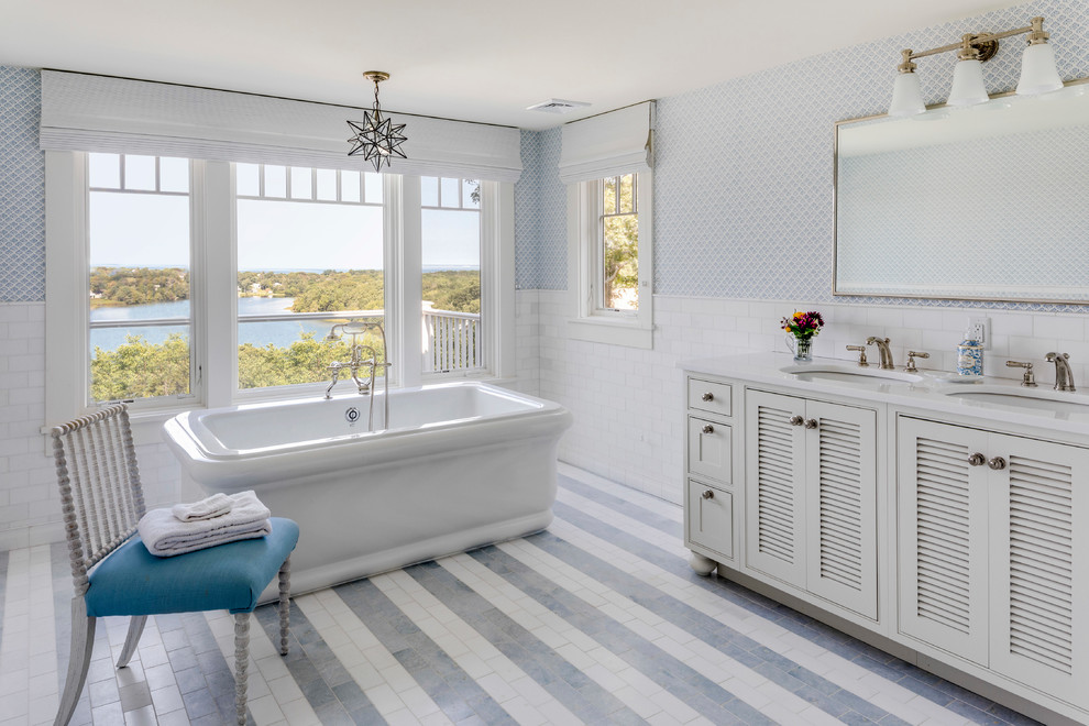 На фото: большая главная ванная комната в морском стиле с фасадами с филенкой типа жалюзи, белыми фасадами, отдельно стоящей ванной, белой плиткой, врезной раковиной, разноцветным полом, плиткой кабанчик, разноцветными стенами и зеркалом с подсветкой с
