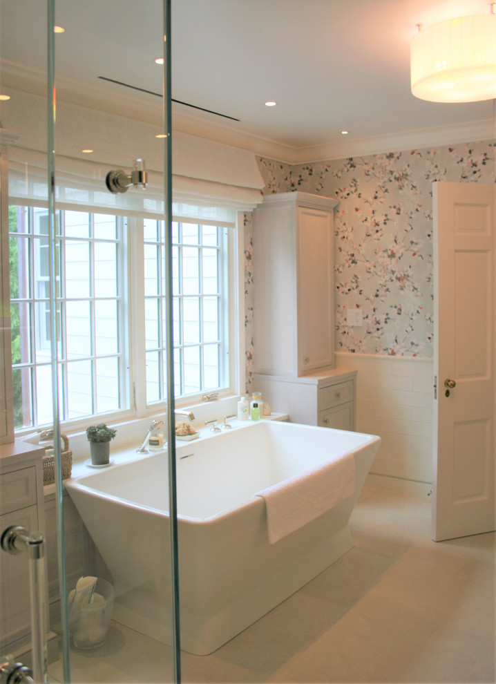 Photo of a large classic ensuite bathroom in New York with freestanding cabinets, light wood cabinets, a freestanding bath, a built-in shower, porcelain flooring, a submerged sink, glass worktops, an open shower, white worktops, double sinks, a built in vanity unit, white tiles, ceramic tiles, multi-coloured walls, beige floors, wallpapered walls, a two-piece toilet and a shower bench.