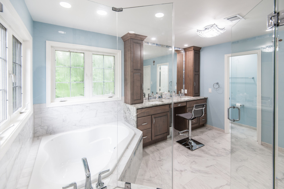 Klassisk inredning av ett stort en-suite badrum, med luckor med upphöjd panel, bruna skåp, ett hörnbadkar, en hörndusch, vit kakel, porslinskakel, blå väggar, klinkergolv i porslin, ett undermonterad handfat, granitbänkskiva och dusch med gångjärnsdörr