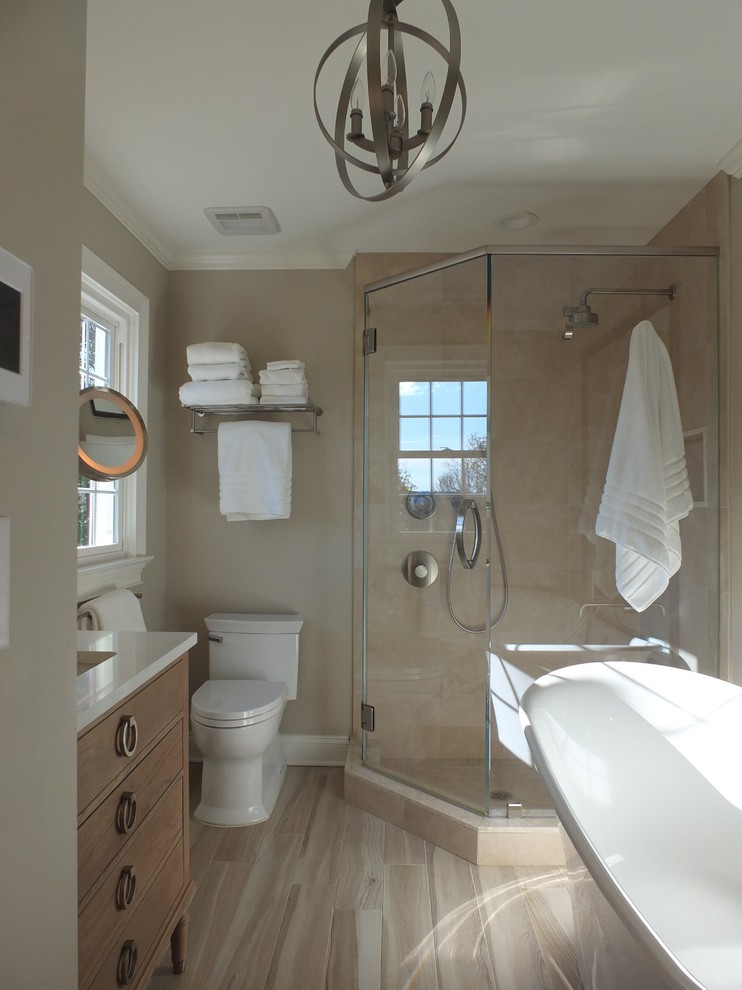 Photo of a large classic ensuite bathroom in New York with flat-panel cabinets, light wood cabinets, a freestanding bath, a corner shower, a one-piece toilet, beige tiles, porcelain tiles, beige walls, ceramic flooring, a submerged sink, engineered stone worktops, brown floors and a hinged door.