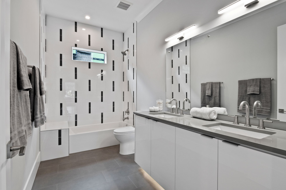 Cette image montre une salle de bain design avec un placard à porte plane, des portes de placard blanches, une baignoire en alcôve, un combiné douche/baignoire, un carrelage blanc, un mur gris, un lavabo encastré, un sol gris, un plan de toilette gris, meuble double vasque et meuble-lavabo suspendu.
