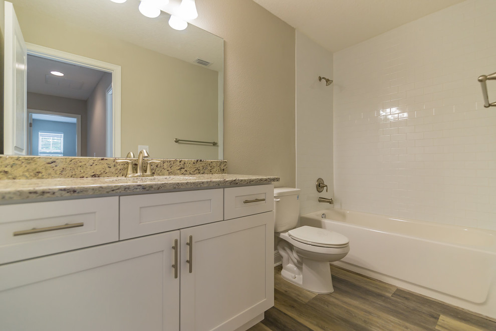Exempel på ett mellanstort klassiskt badrum för barn, med skåp i shakerstil, vita skåp, ett badkar i en alkov, en dusch/badkar-kombination, vit kakel, keramikplattor, laminatgolv, granitbänkskiva, grått golv och dusch med duschdraperi