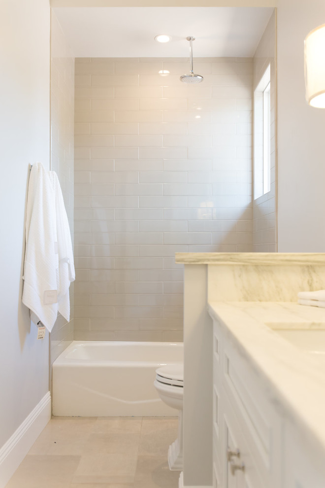 Klassisk inredning av ett stort badrum med dusch, med vita skåp, ett badkar i en alkov, en toalettstol med hel cisternkåpa, grå väggar, ett undermonterad handfat, tunnelbanekakel, luckor med infälld panel, marmorbänkskiva, grått golv, dusch med duschdraperi, en dusch/badkar-kombination, vit kakel och klinkergolv i porslin