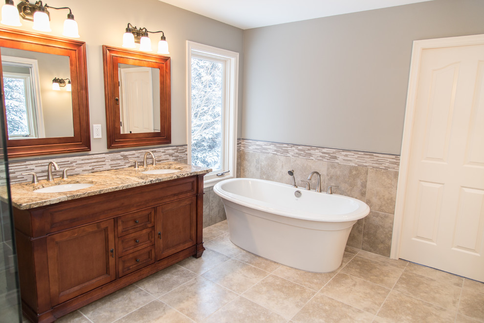 This is an example of a large classic ensuite bathroom in Calgary with a submerged sink, granite worktops, a freestanding bath, beige tiles, cement tiles, grey walls, ceramic flooring, beige floors, a hinged door, recessed-panel cabinets, medium wood cabinets and a corner shower.