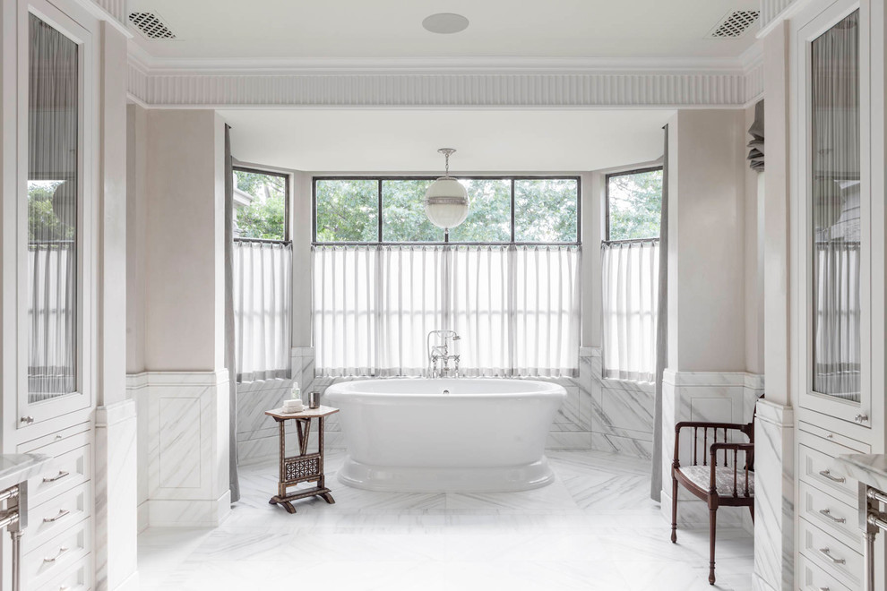 Inspiration pour une salle de bain principale traditionnelle avec des portes de placard blanches, une baignoire indépendante, un mur beige, un sol blanc, une fenêtre et un placard avec porte à panneau encastré.