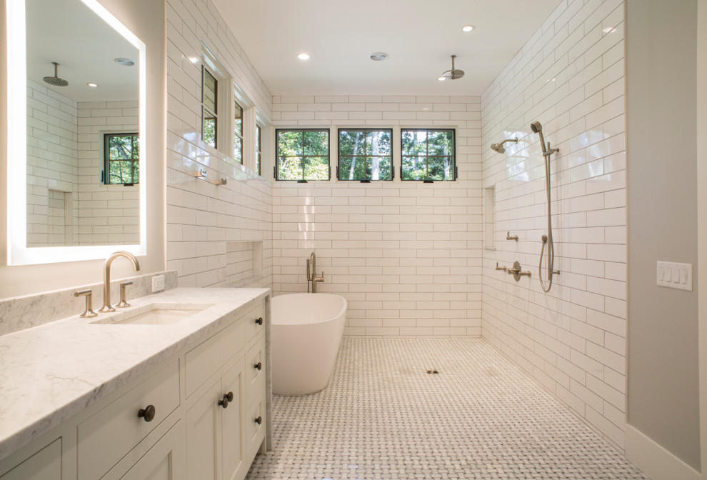 Klassisk inredning av ett stort en-suite badrum, med luckor med infälld panel, vita skåp, ett fristående badkar, en öppen dusch, en toalettstol med hel cisternkåpa, vit kakel, tunnelbanekakel, beige väggar och med dusch som är öppen