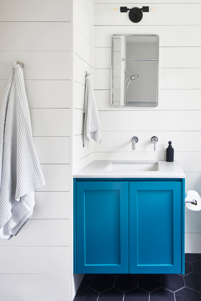 Cette image montre une salle de bain traditionnelle de taille moyenne avec un placard à porte shaker, des portes de placard bleues, un mur blanc, un lavabo encastré, un sol noir et un plan de toilette blanc.