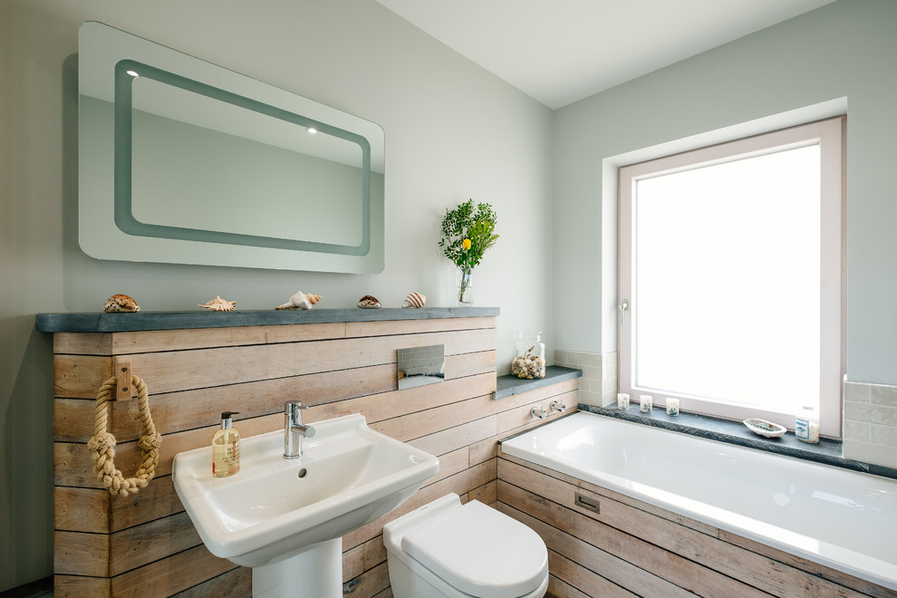 Diseño de cuarto de baño principal costero con bañera encastrada, sanitario de pared, paredes azules y lavabo con pedestal