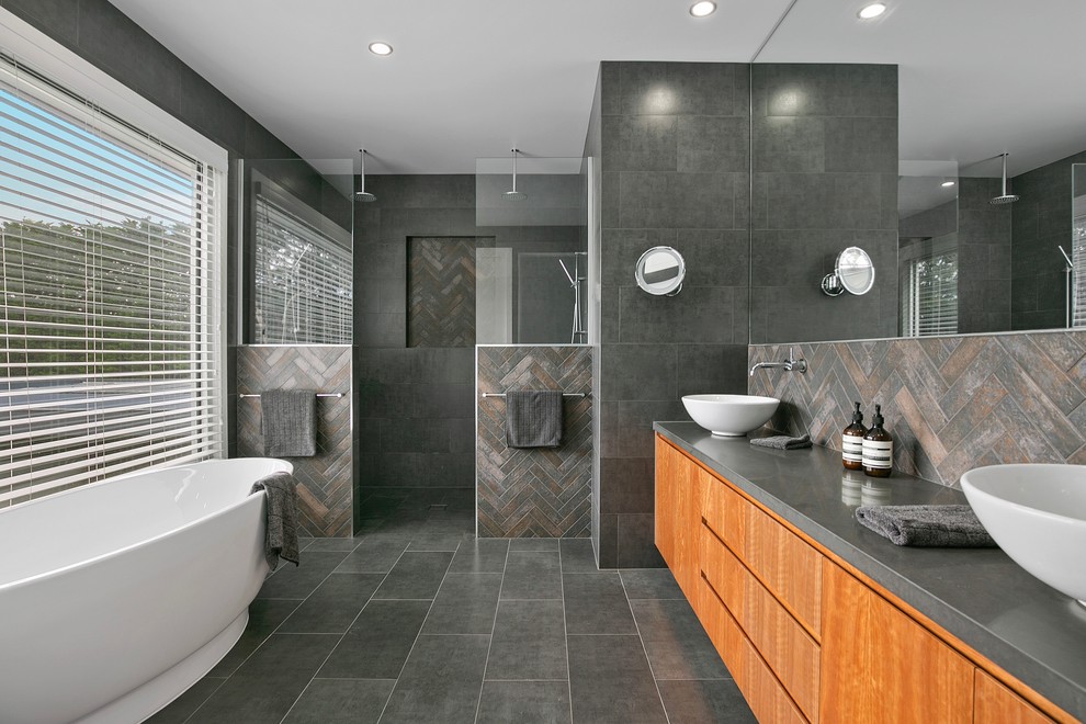 Expansive contemporary ensuite bathroom in Geelong with flat-panel cabinets, medium wood cabinets, a freestanding bath, a walk-in shower, grey tiles, ceramic tiles, grey walls, ceramic flooring, a vessel sink and engineered stone worktops.