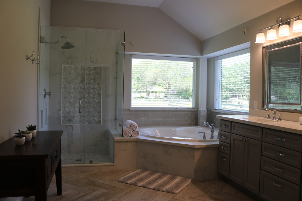 Photo of a classic ensuite bathroom in Houston with grey cabinets, a built-in bath, grey tiles, marble tiles, grey walls, porcelain flooring, a submerged sink, engineered stone worktops, grey floors, a hinged door, white worktops and recessed-panel cabinets.