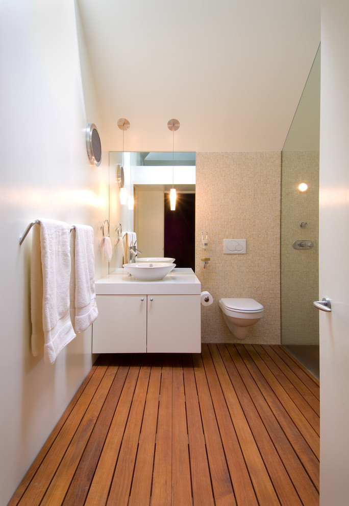 Idéer för funkis badrum, med ett fristående handfat, släta luckor, vita skåp, bänkskiva i akrylsten, en kantlös dusch, en vägghängd toalettstol, beige kakel och mosaik