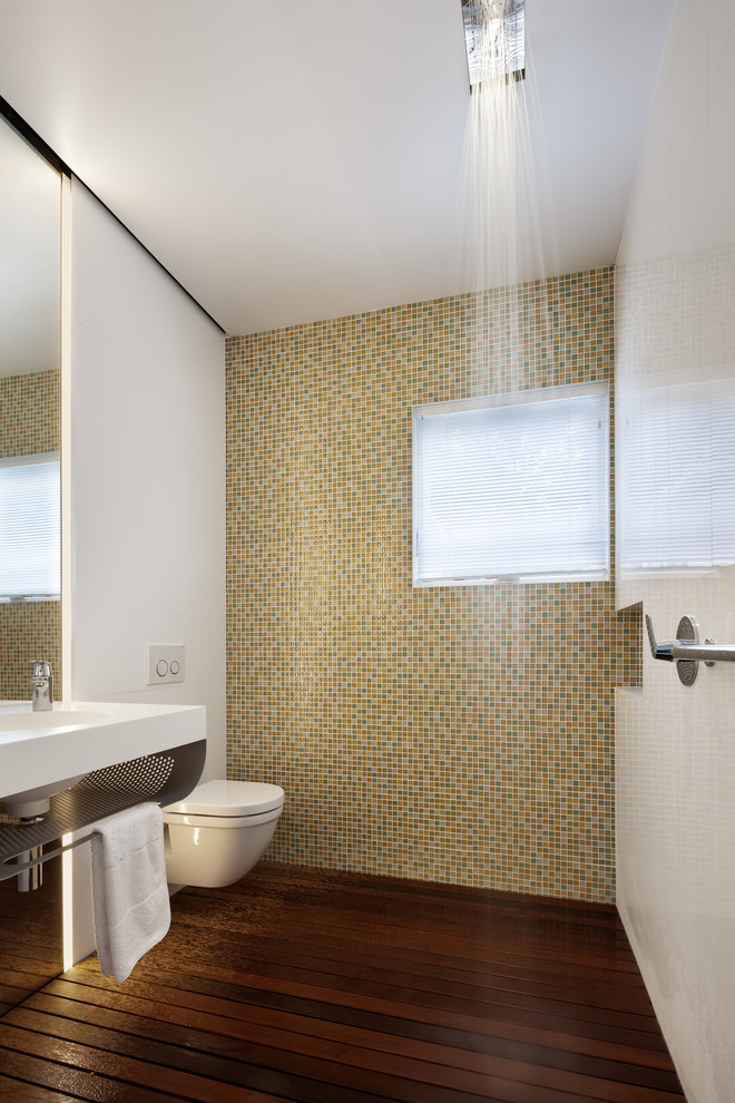 Bild på ett litet funkis badrum, med bänkskiva i akrylsten, en vägghängd toalettstol, flerfärgad kakel, mosaik, vita väggar, mörkt trägolv och en kantlös dusch