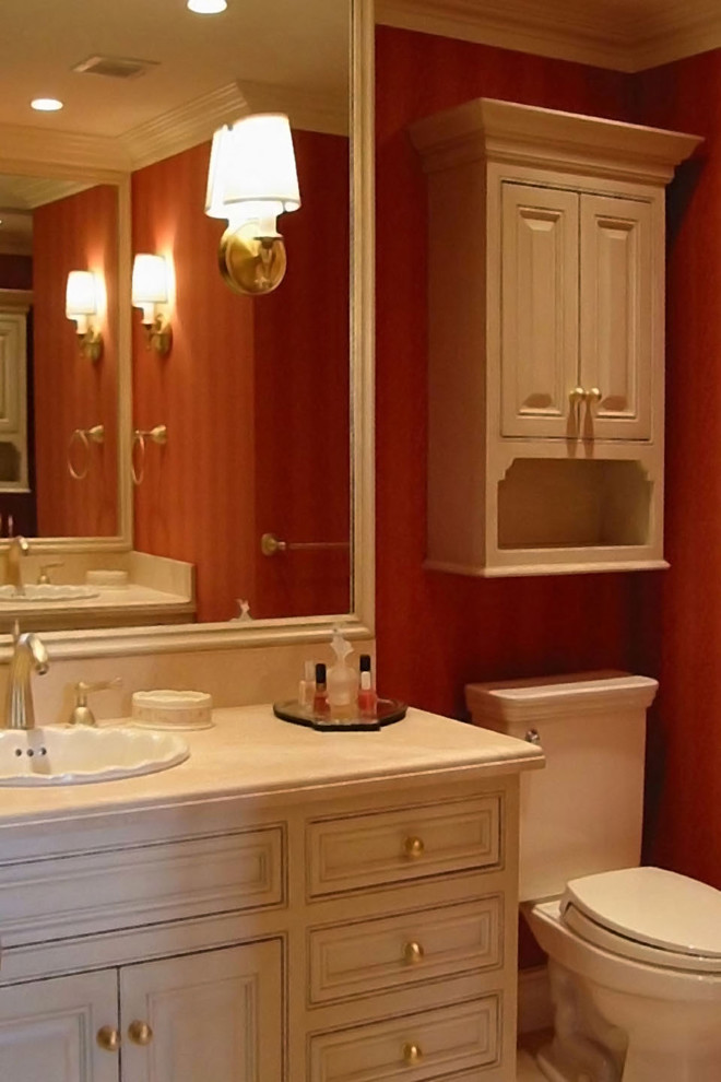 ボストンにある広いトラディショナルスタイルのおしゃれな浴室 (フラットパネル扉のキャビネット、白いキャビネット、アンダーマウント型浴槽、一体型トイレ	、赤い壁、ライムストーンの床、オーバーカウンターシンク、ライムストーンの洗面台、ベージュの床) の写真