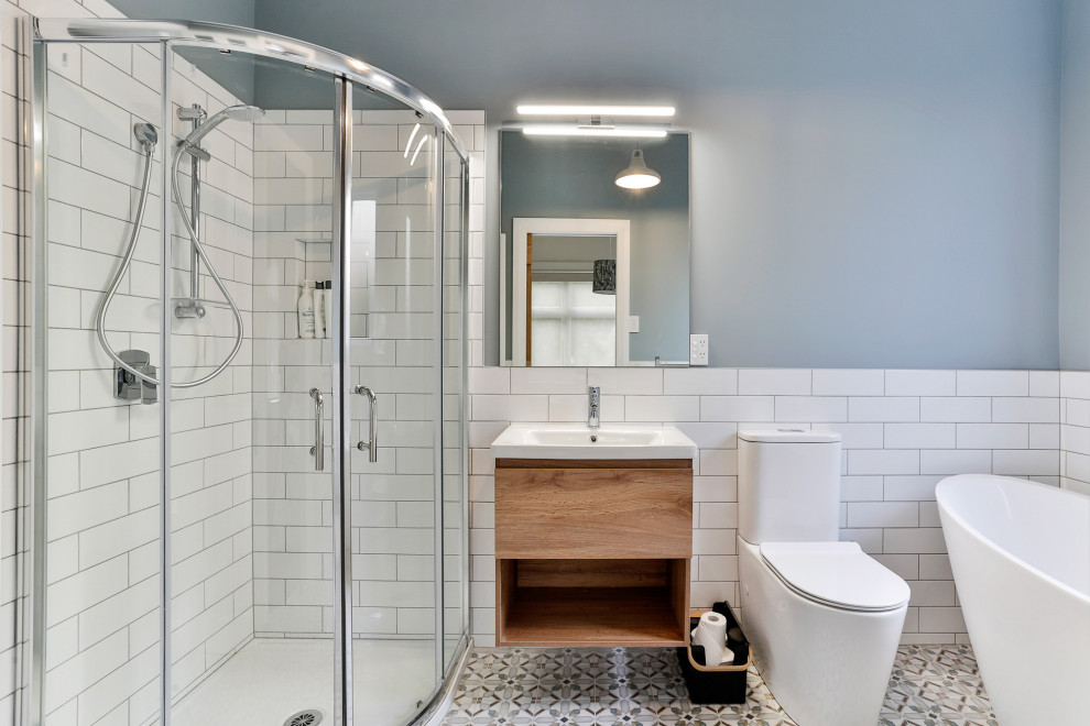 Пример оригинального дизайна: большая главная ванная комната в классическом стиле с фасадами цвета дерева среднего тона, отдельно стоящей ванной, угловым душем, унитазом-моноблоком, белой плиткой, керамической плиткой, синими стенами, полом из мозаичной плитки, подвесной раковиной, разноцветным полом, душем с раздвижными дверями и белой столешницей