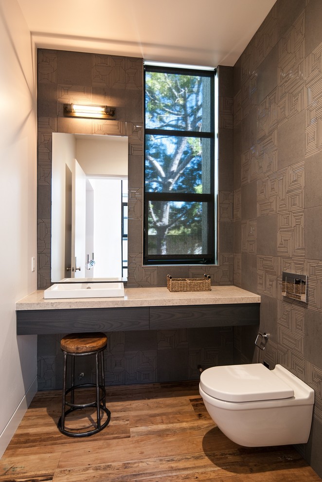 Cette photo montre une salle d'eau moderne de taille moyenne avec des carreaux de porcelaine, un placard à porte plane, des portes de placard noires, un bidet, un mur gris, parquet clair, un lavabo posé et un plan de toilette en granite.
