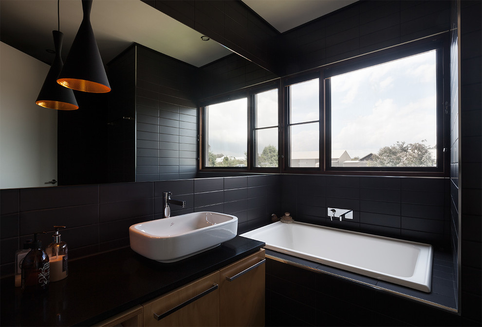 Modelo de cuarto de baño principal contemporáneo con lavabo sobreencimera, armarios tipo mueble, puertas de armario de madera clara, bañera encastrada, baldosas y/o azulejos negros y paredes negras