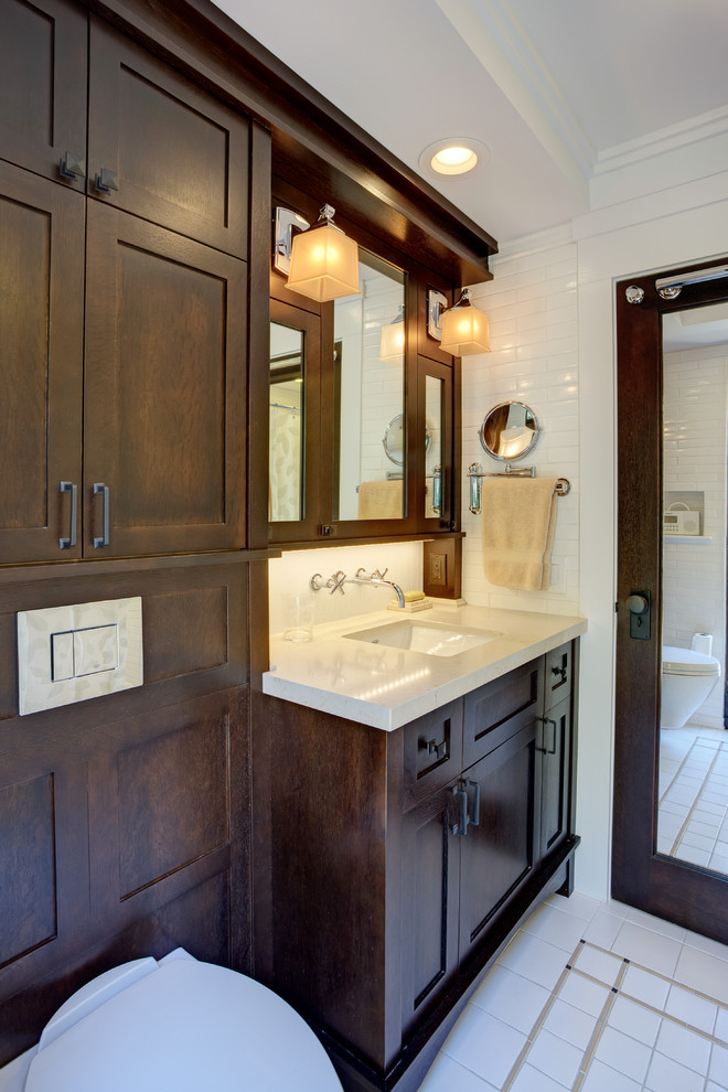 Exemple d'une petite salle de bain principale chic en bois foncé avec un lavabo encastré, un placard à porte shaker, un plan de toilette en surface solide, une baignoire en alcôve, WC suspendus, un carrelage blanc, des carreaux de céramique, un mur blanc, un sol en carrelage de céramique, un combiné douche/baignoire et un sol blanc.