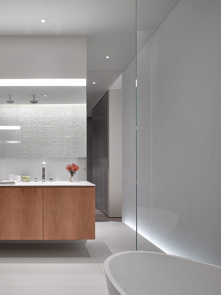 Photo of a contemporary bathroom in New York with flat-panel cabinets, medium wood cabinets, a freestanding bath, grey walls, white floors and white worktops.