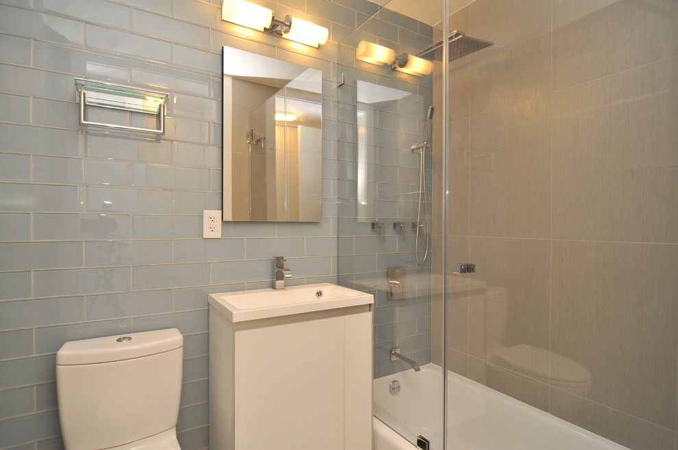 Aménagement d'une salle d'eau contemporaine de taille moyenne avec un placard à porte plane, des portes de placard blanches, une baignoire en alcôve, un combiné douche/baignoire, WC à poser, un carrelage bleu, un carrelage en pâte de verre, un mur beige, un lavabo intégré, un plan de toilette en surface solide, une cabine de douche à porte battante, sol en stratifié et un sol beige.