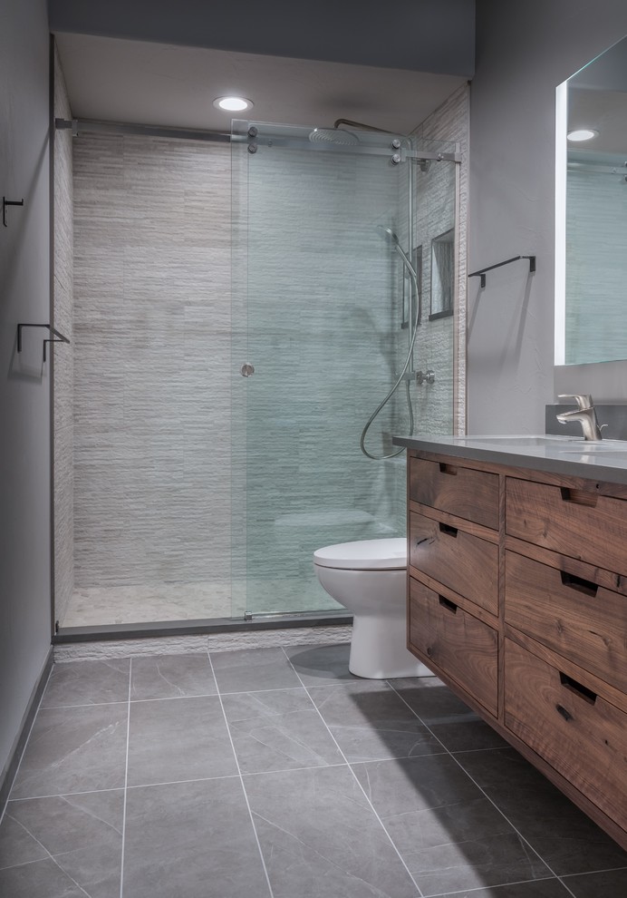Exemple d'une salle de bain tendance en bois brun de taille moyenne avec un placard à porte plane, WC à poser, un mur bleu, un sol en carrelage de céramique, un lavabo encastré, un plan de toilette en quartz modifié, une cabine de douche à porte coulissante, un carrelage blanc, des carreaux de céramique et un sol gris.