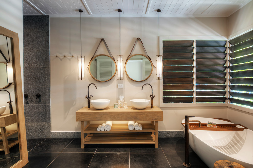 Inredning av ett exotiskt en-suite badrum, med öppna hyllor, skåp i ljust trä, ett fristående badkar, en öppen dusch, grå kakel, ett fristående handfat, träbänkskiva, svart golv och med dusch som är öppen