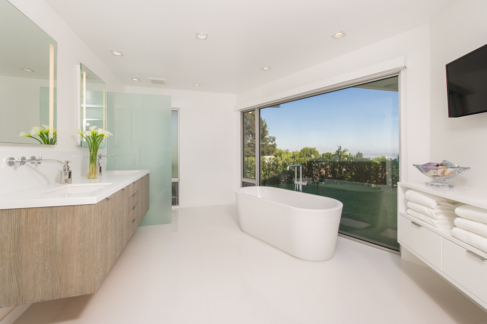Стильный дизайн: ванная комната в современном стиле с врезной раковиной, плоскими фасадами, светлыми деревянными фасадами, отдельно стоящей ванной и белыми стенами - последний тренд