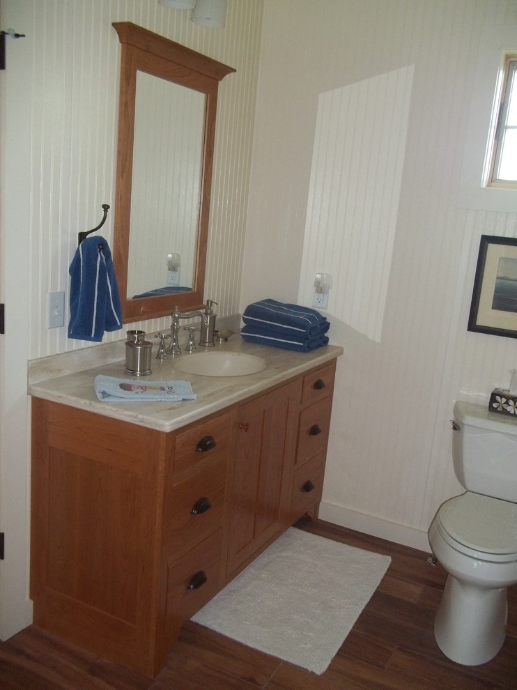 Example of a mid-sized farmhouse medium tone wood floor bathroom design in New York with shaker cabinets, light wood cabinets, solid surface countertops and white walls