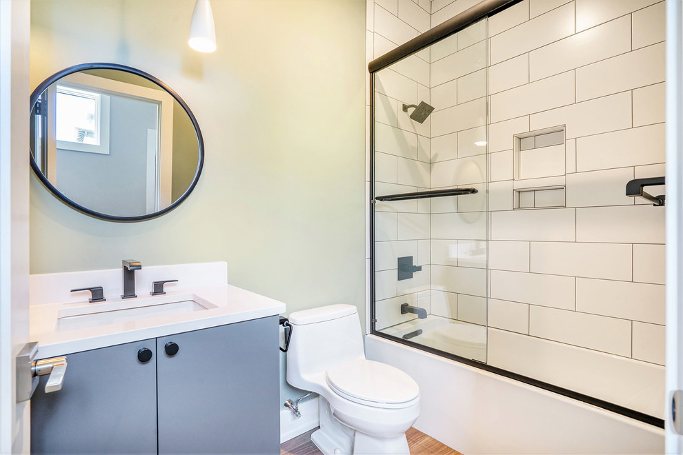 Modern inredning av ett mellanstort vit vitt badrum med dusch, med släta luckor, grå skåp, ett platsbyggt badkar, en dusch/badkar-kombination, en toalettstol med hel cisternkåpa, tunnelbanekakel, mellanmörkt trägolv, ett undermonterad handfat, bänkskiva i akrylsten, brunt golv och dusch med skjutdörr