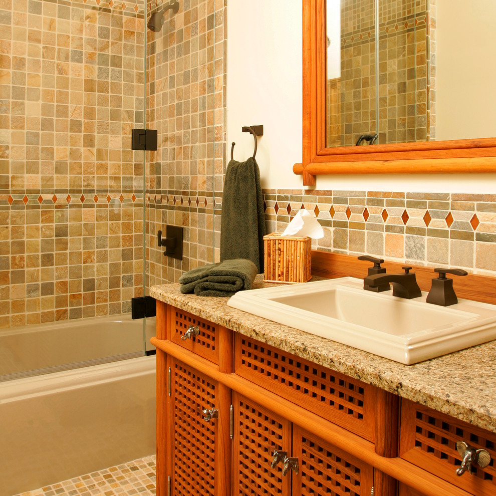 На фото: ванная комната в классическом стиле с накладной раковиной, фасадами цвета дерева среднего тона, столешницей из гранита, ванной в нише, душем над ванной, разноцветной плиткой, белыми стенами, каменной плиткой, полом из известняка и плоскими фасадами с