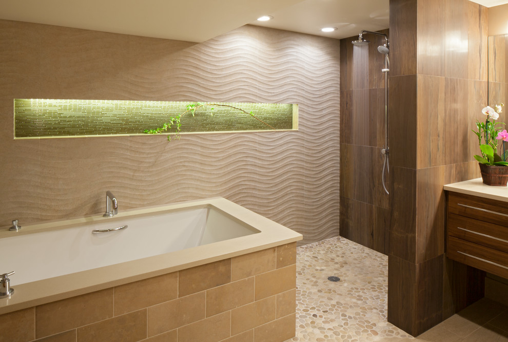 Inredning av ett modernt en-suite badrum, med släta luckor, skåp i mellenmörkt trä, bänkskiva i kvartsit, ett undermonterat badkar, en dubbeldusch, brun kakel, beige väggar och klinkergolv i småsten
