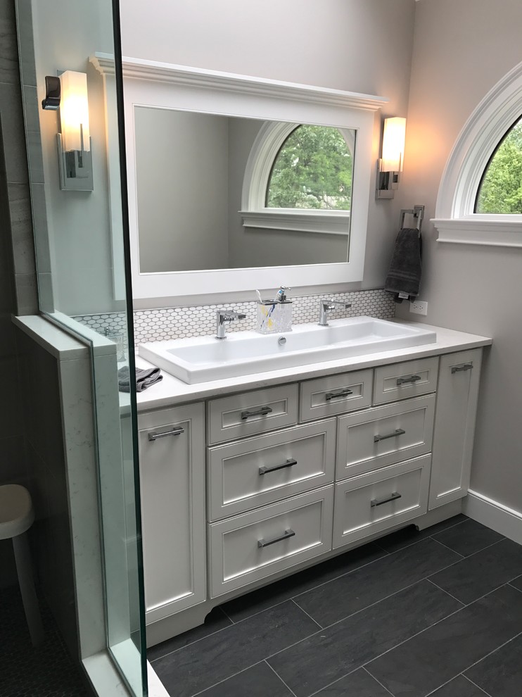 Corner shower - mid-sized traditional master gray tile and porcelain tile porcelain tile and gray floor corner shower idea in Chicago with recessed-panel cabinets, white cabinets, a two-piece toilet, gray walls, a trough sink, quartz countertops and a hinged shower door