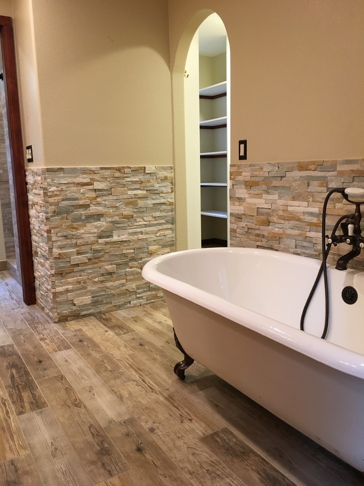 Cette image montre une salle de bain principale rustique de taille moyenne avec une baignoire sur pieds, un carrelage beige, un carrelage de pierre, un mur beige, un sol en bois brun et un sol marron.