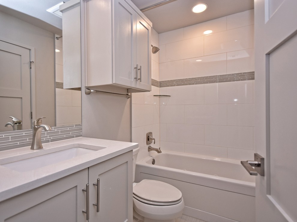 Cette photo montre une petite salle de bain tendance avec des portes de placard blanches, une baignoire en alcôve, WC séparés, un carrelage blanc, un carrelage en pâte de verre, un mur gris, un sol en carrelage de porcelaine, un lavabo encastré, un plan de toilette en quartz modifié et un placard avec porte à panneau encastré.